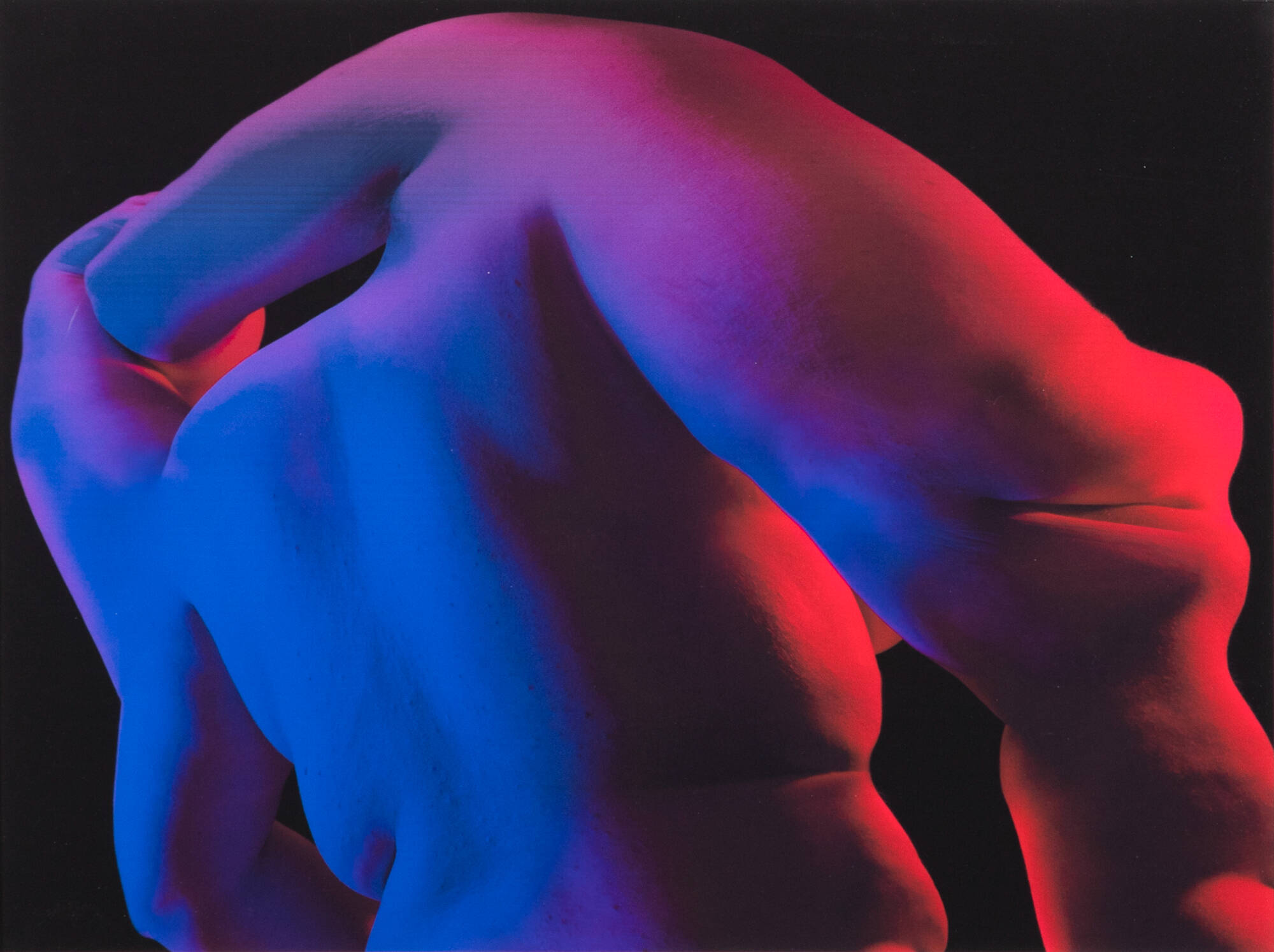 Digital photograph of two bodies, merging into one, colored by blue and red lights against a dark background.